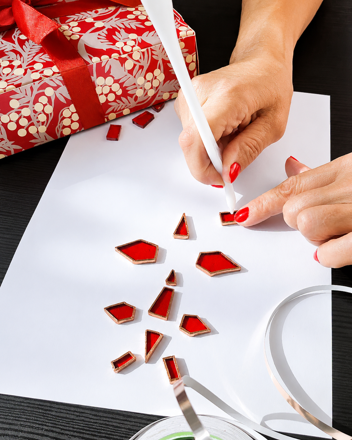 Maria Avram burnishing copper foil around hand-cut red stained glass pieces using the Tiffany method.