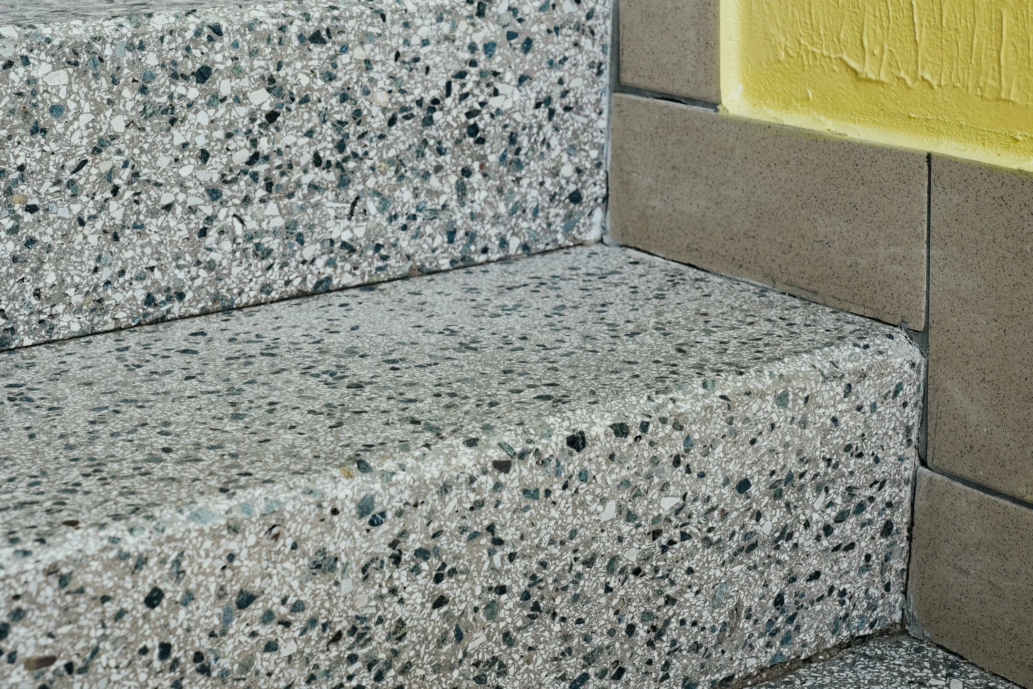 Close-up of terrazzo stairs with yellow-painted wall and beige tile detail.