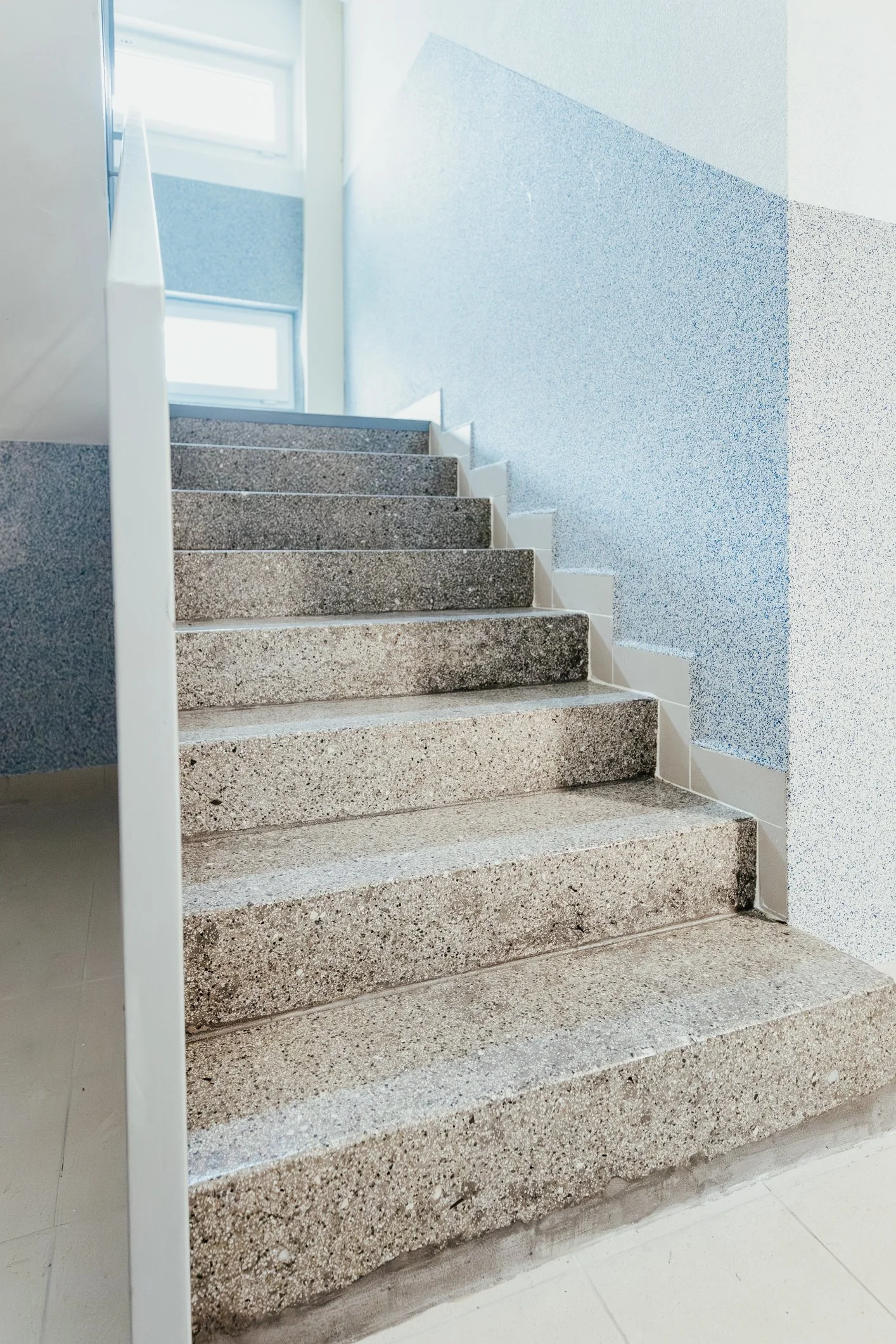 Concrete staircase with blue speckled walls and white handrail, natural light from windows at the top.