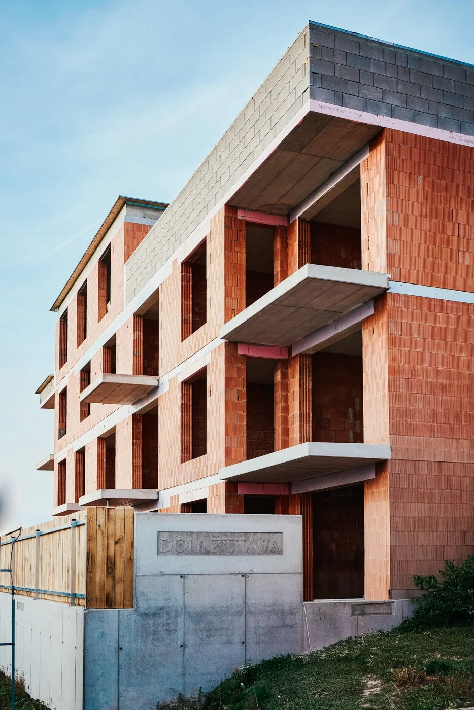 Unfinished brick building with open balconies and concrete elements under construction against a clear sky.