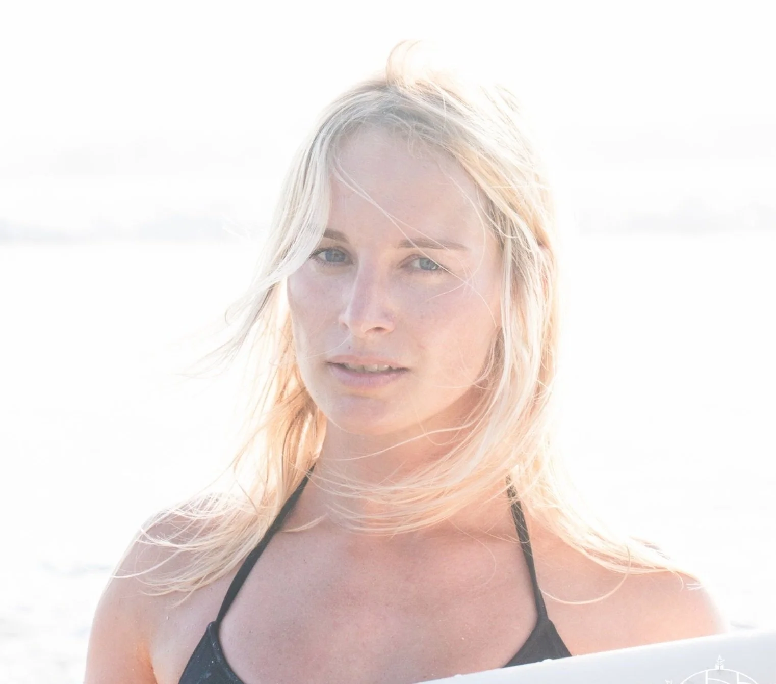 Woman with blonde hair at the beach in a black swimsuit.