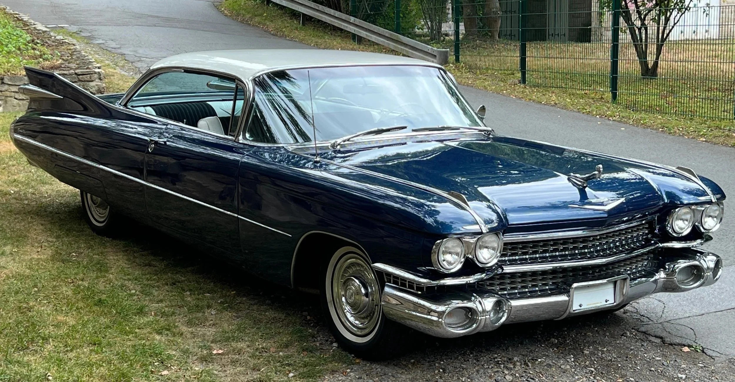 Ein klassischer dunkelblauer Cadillac aus den 1960er Jahren, geparkt auf einem Rasen neben einer Straße.