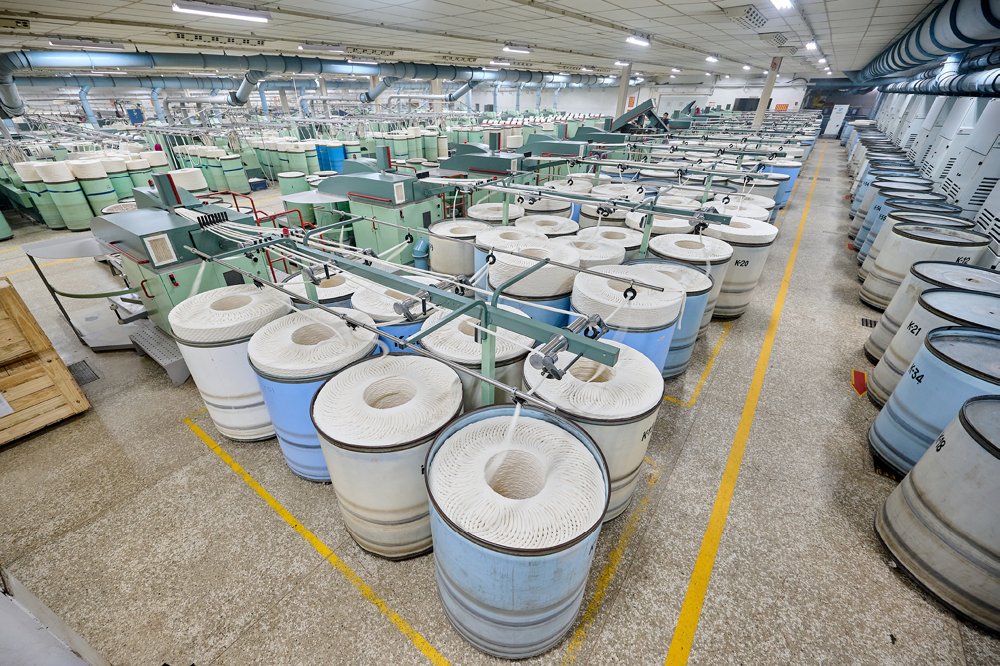 Industrial textile manufacturing facility with large spinning or dyeing machines and numerous spools of yarn or thread.