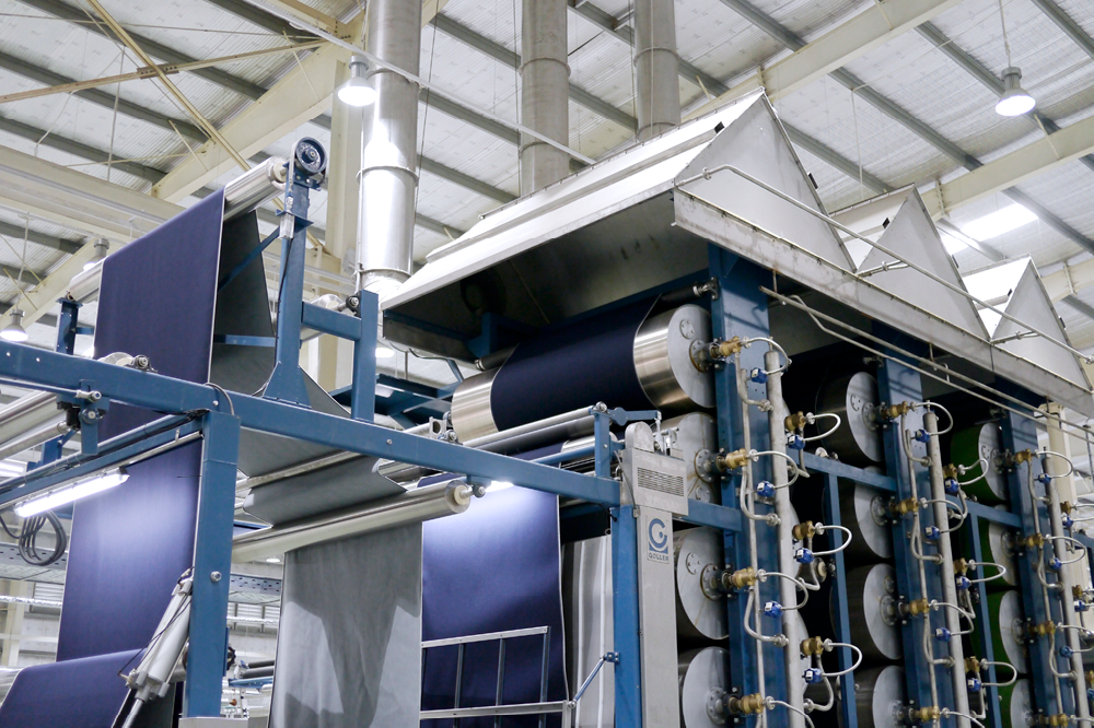 Industrial manufacturing equipment with rollers, belts, and metal structures in a factory setting.