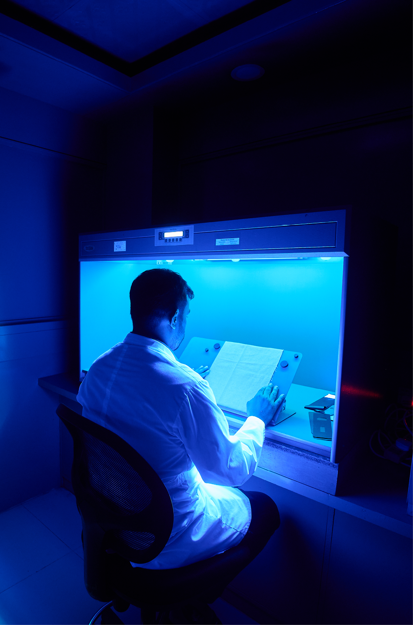 A man in a white lab coat working under blue light in a biological safety cabinet in a laboratory.