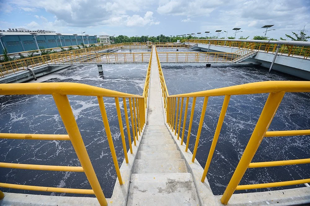A view of a water treatment plant with aeration tanks and yellow safety railings, under a cloudy sky.