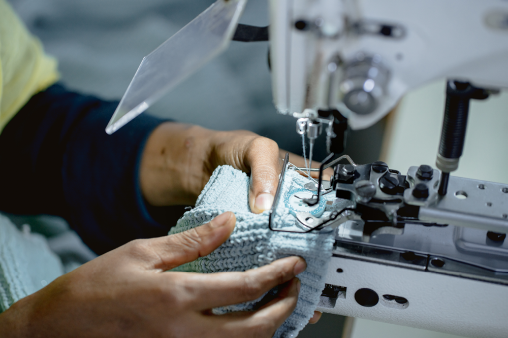 A person operating a sewing machine to stitch fabric with a cloth in a factory or workshop.