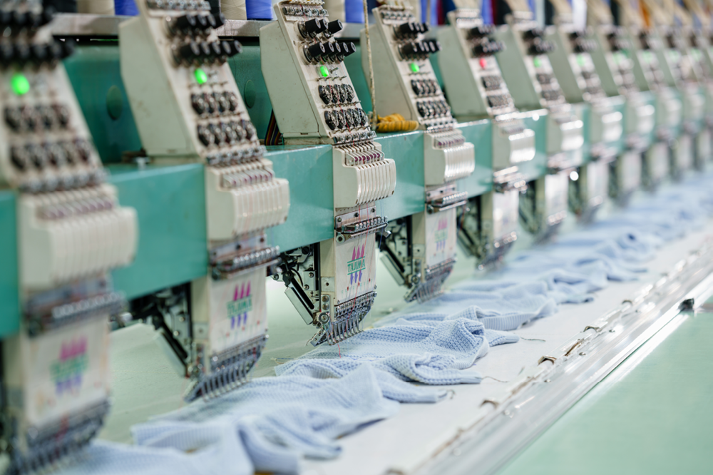 Multiple industrial embroidery machines stitching shirts in a factory setting.