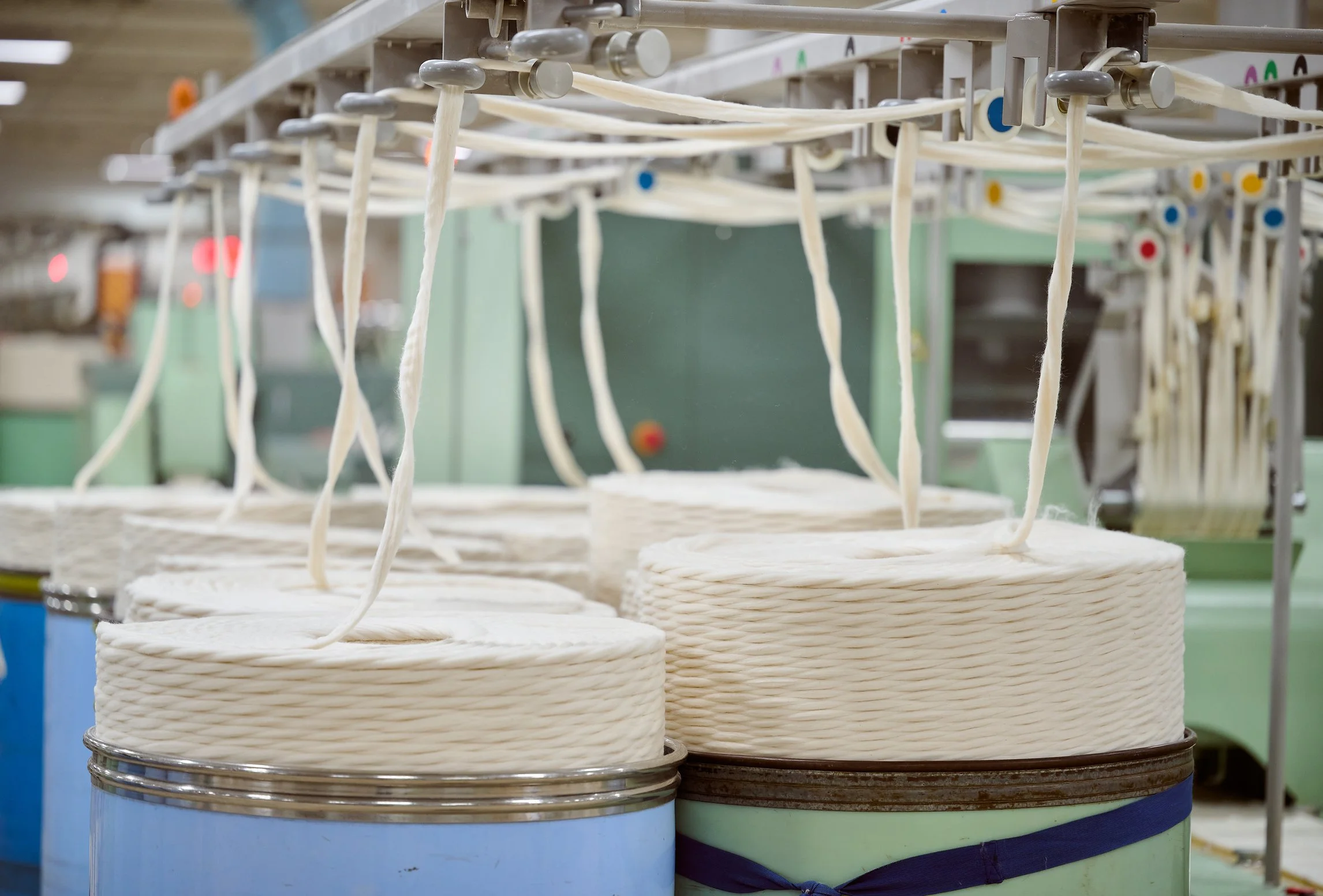 Industrial setting with large rolls of white yarn hanging from drying racks.
