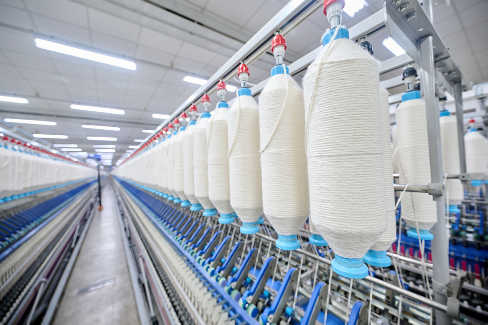 Rows of large spools of white yarn on industrial spinning machines in a textile factory.