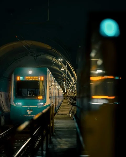 A modern train arriving at an underground station, viewed from the platform with tunnel walls and lighting in the background.