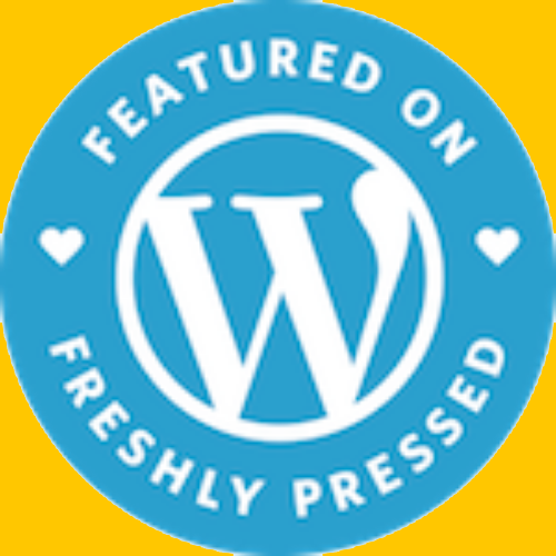 Blue circular badge with white text and logo, reading 'Featured on WordPress, Freshly Pressed' with small heart icons on each side.