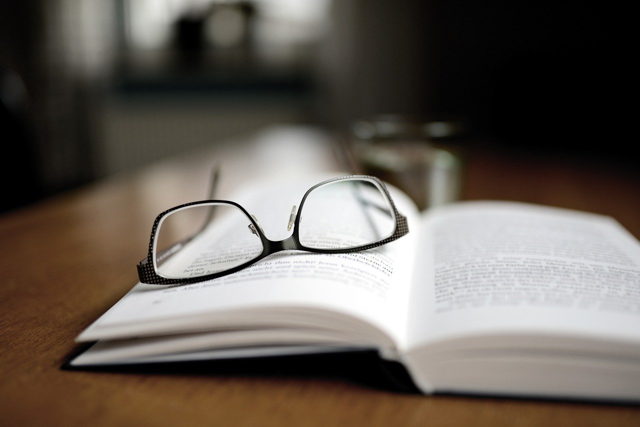 A photo of a pair of glasses lying atop an open book.