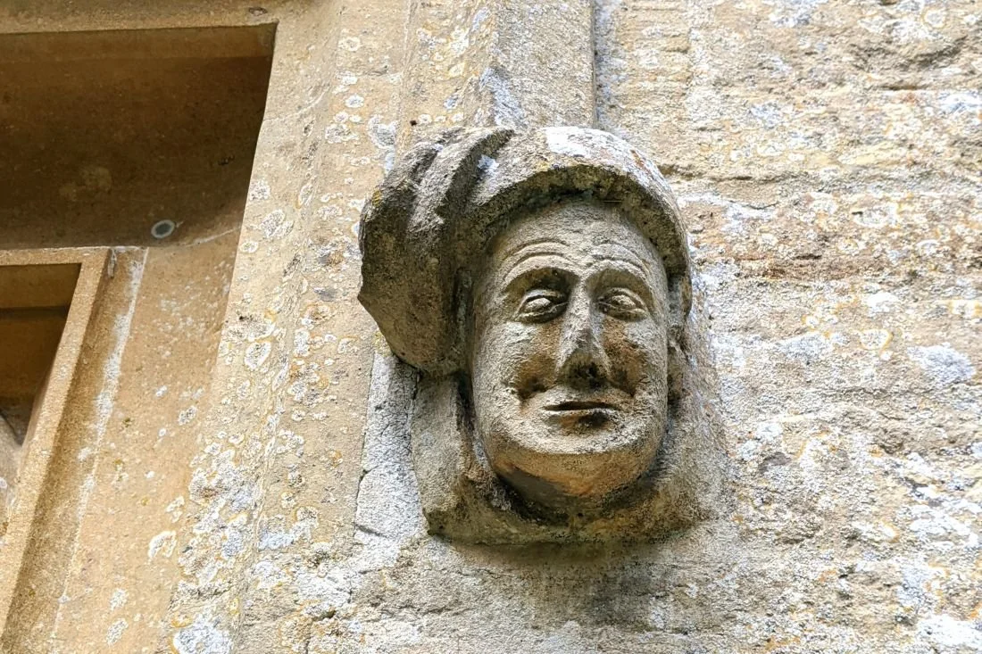 Photo of a carved, medieval face on the side of a stone wall.