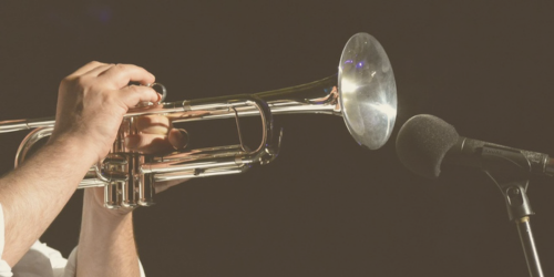 Photo of someone holding a golden trumpet up to a microphone.