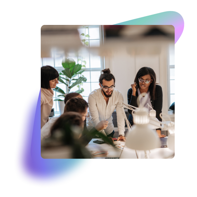 Group of young professionals working together in a bright, modern office space with large windows and plants.