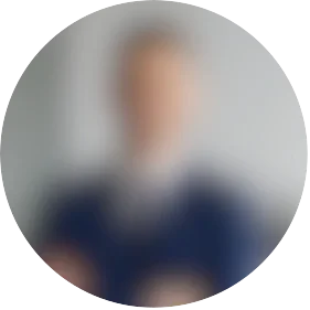 A blurred portrait of a person wearing a dark blazer and holding books or documents.