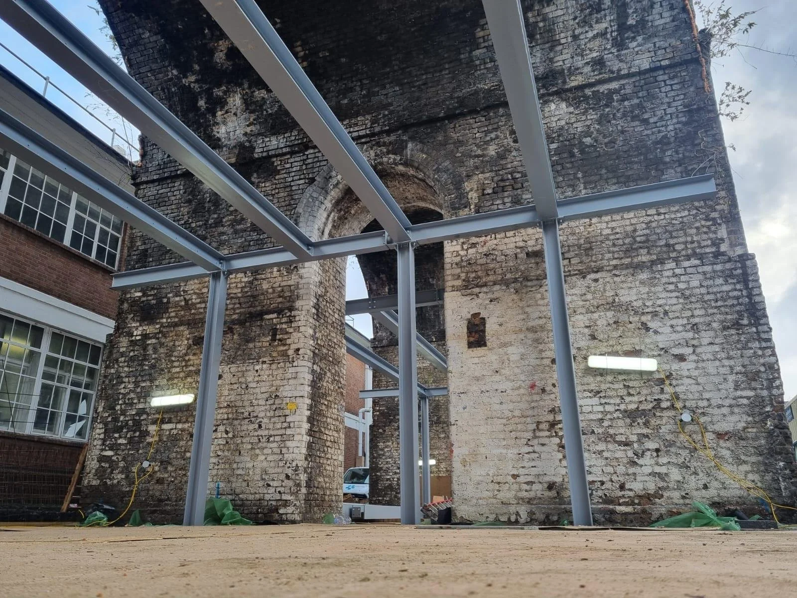 Historic weathered brick building with arched openings and newly installed steel roof framing.