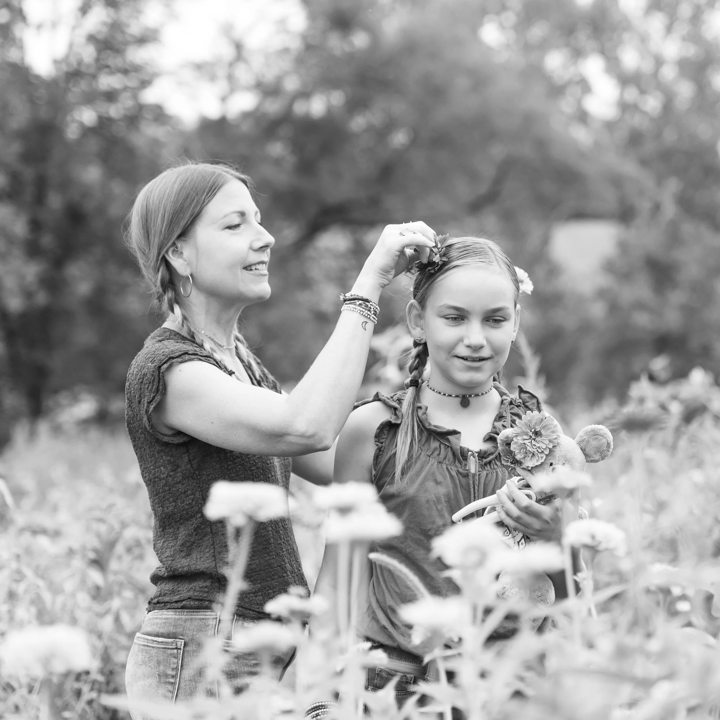 Parenting Astrologer, Tara Vogel, placing a flower in a young girl's hair in a field of flowers, both smiling, black and white photo.