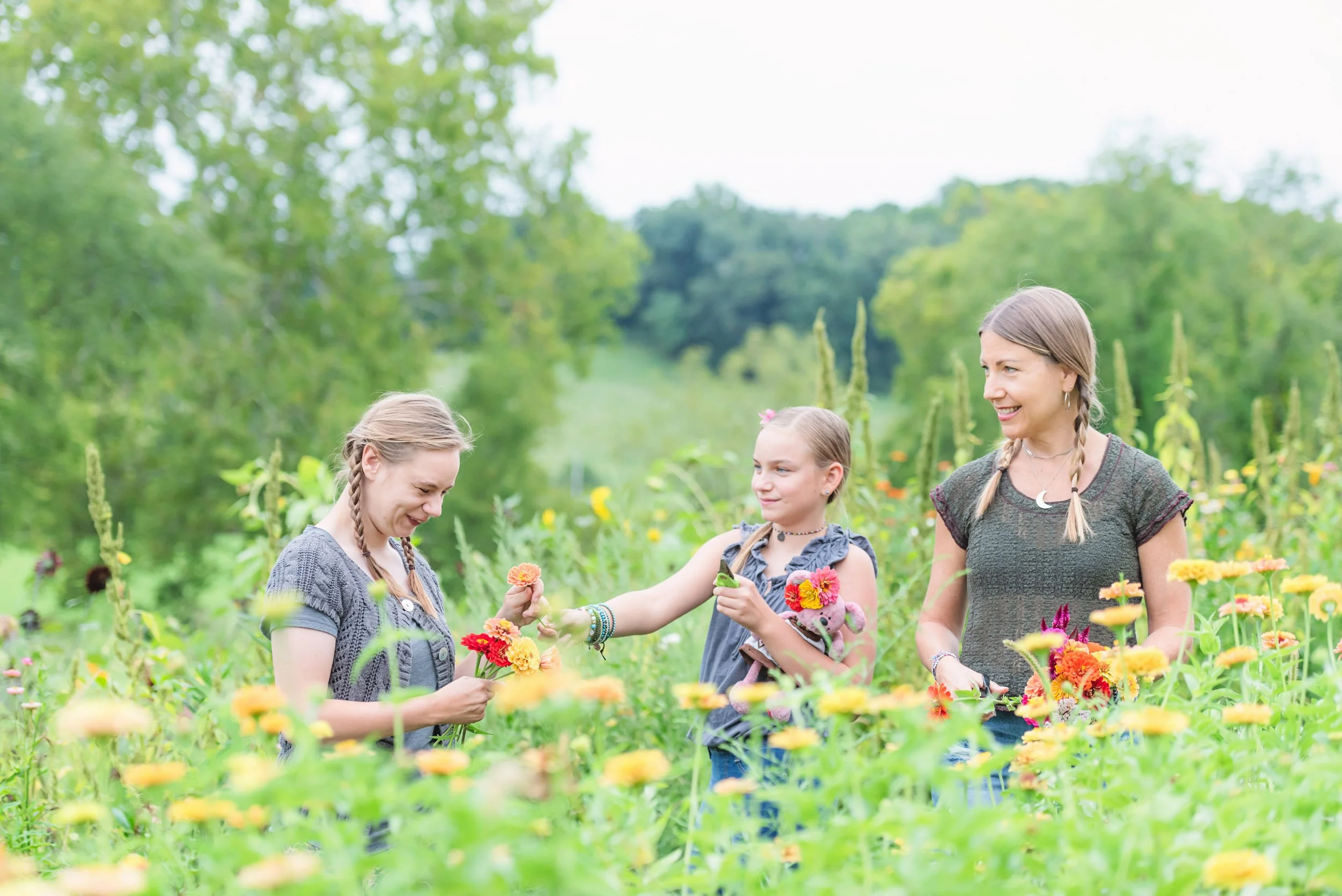 Three women and a girl in a flower field, smiling and interacting with flowers, surrounded by greenery.