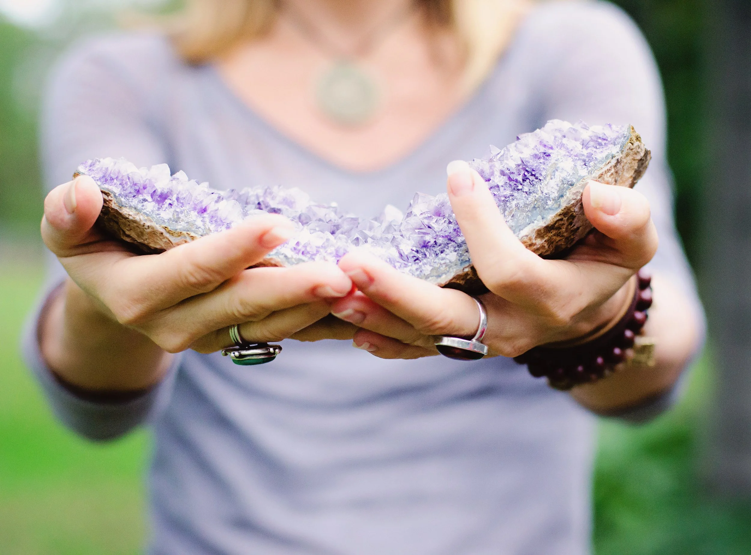 Parenting Astrologer Tara Vogel holding a large, rough, purple-and-white mineral or crystal outdoors.