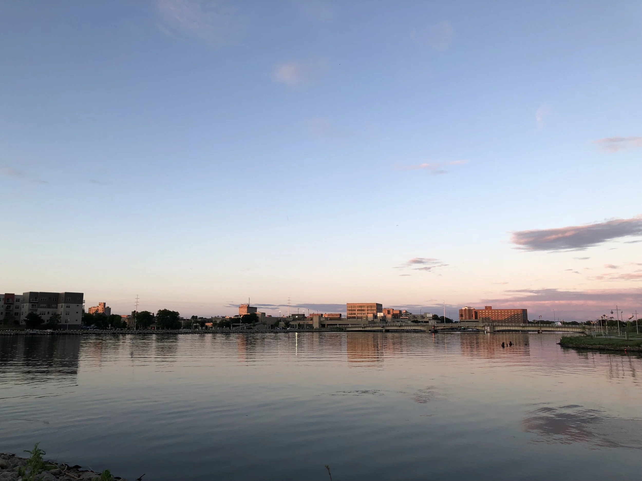 Calm river reflecting city buildings and a colorful sunrise or sunset sky.