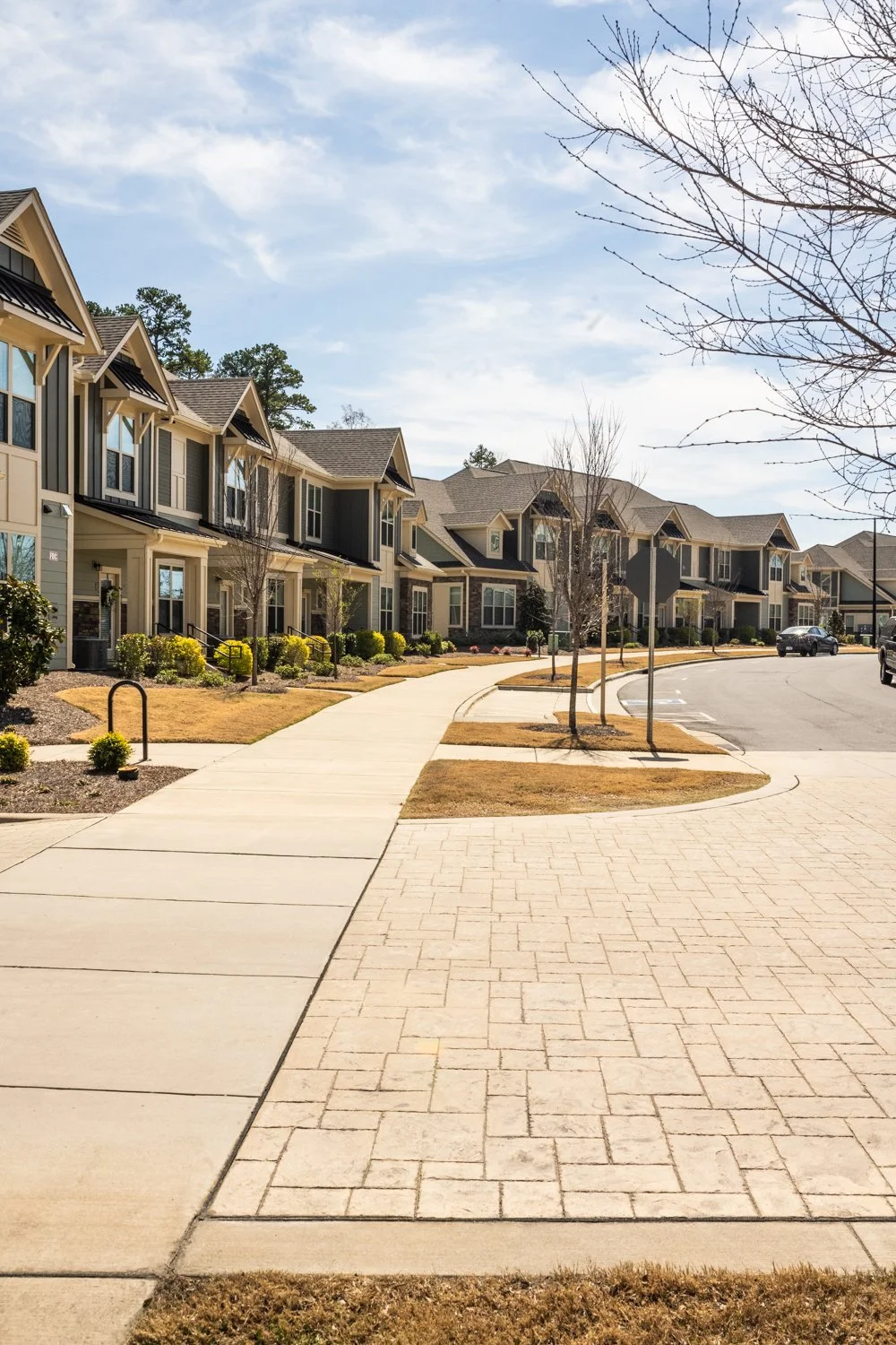 Row of modern townhouses with manicured lawns, sidewalk, and clear blue sky.