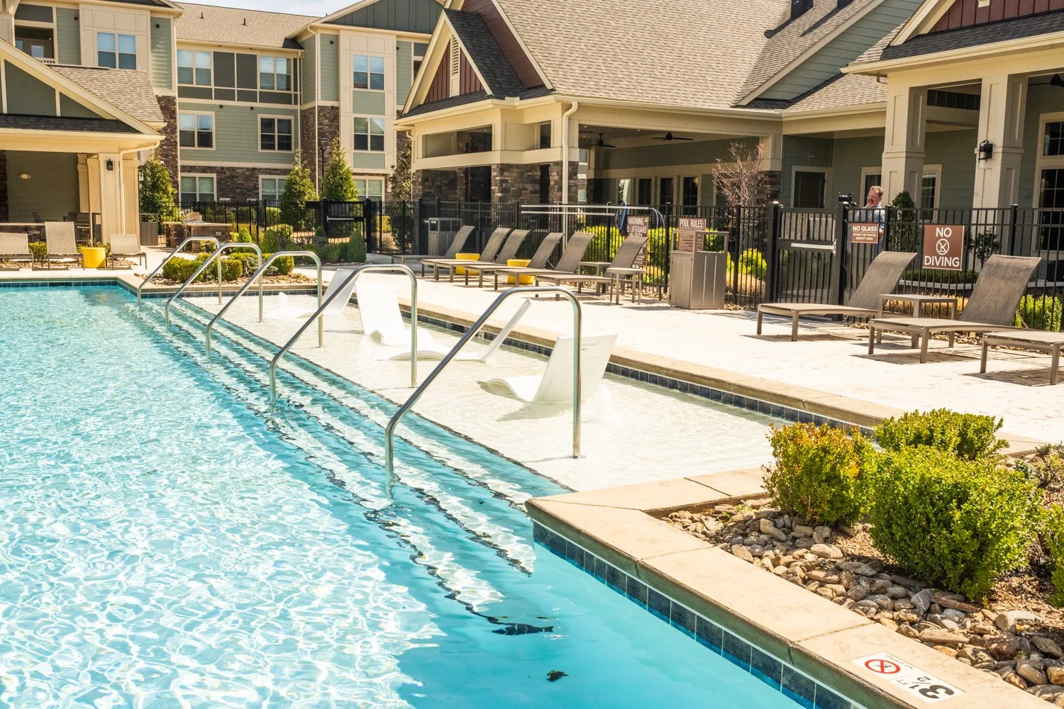 Outdoor swimming pool with lounge chairs, deck, and apartment buildings in the background.