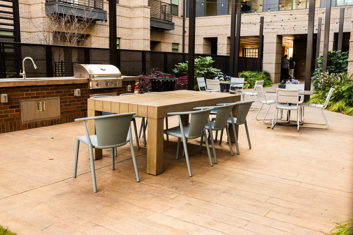 Outdoor patio with a wooden table and chairs, a barbecue grill, and string lights in a courtyard setting.