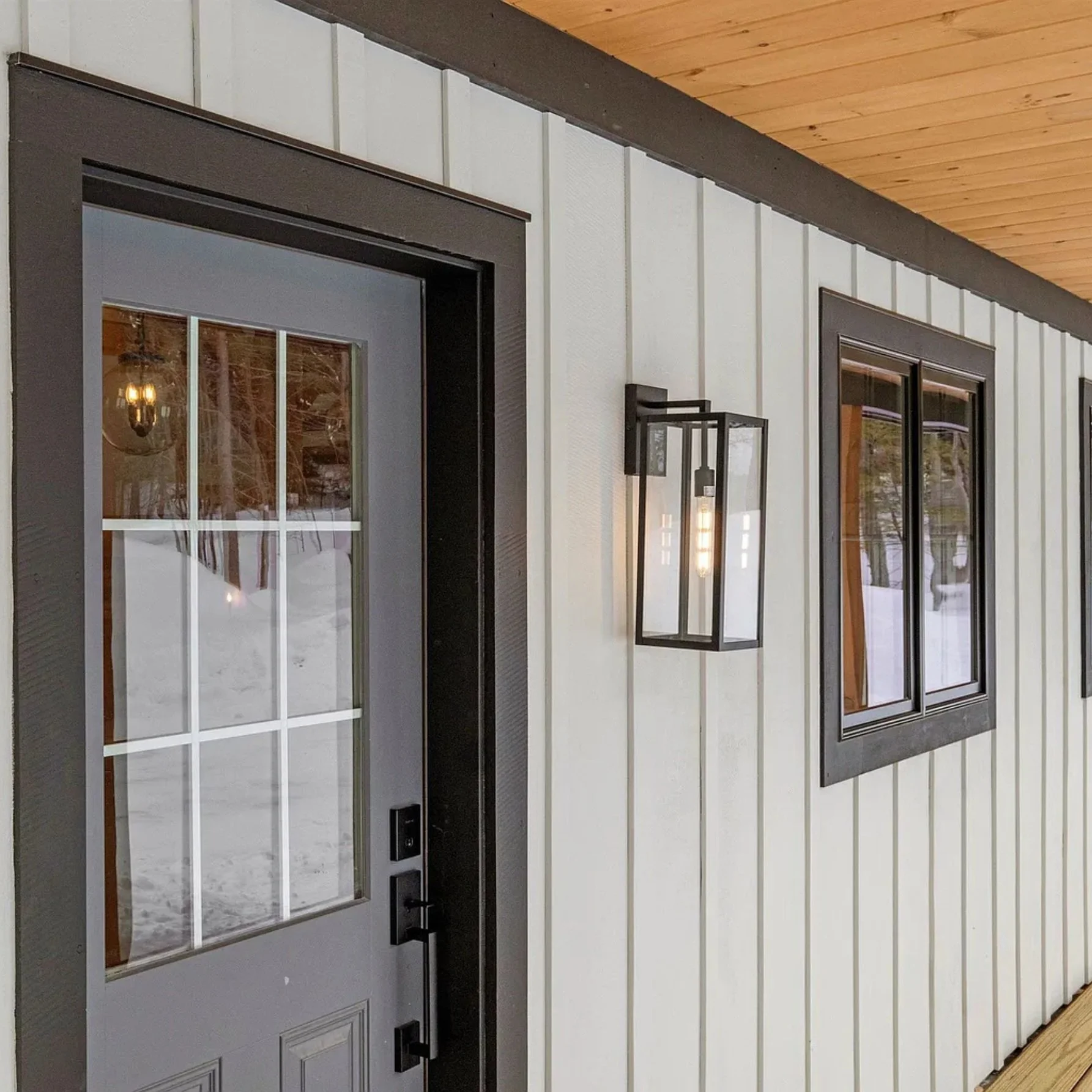 Modern farmhouse exterior with vertical white paneling, black-framed windows, a black-framed door with glass panels, and a wall-mounted lantern light.
