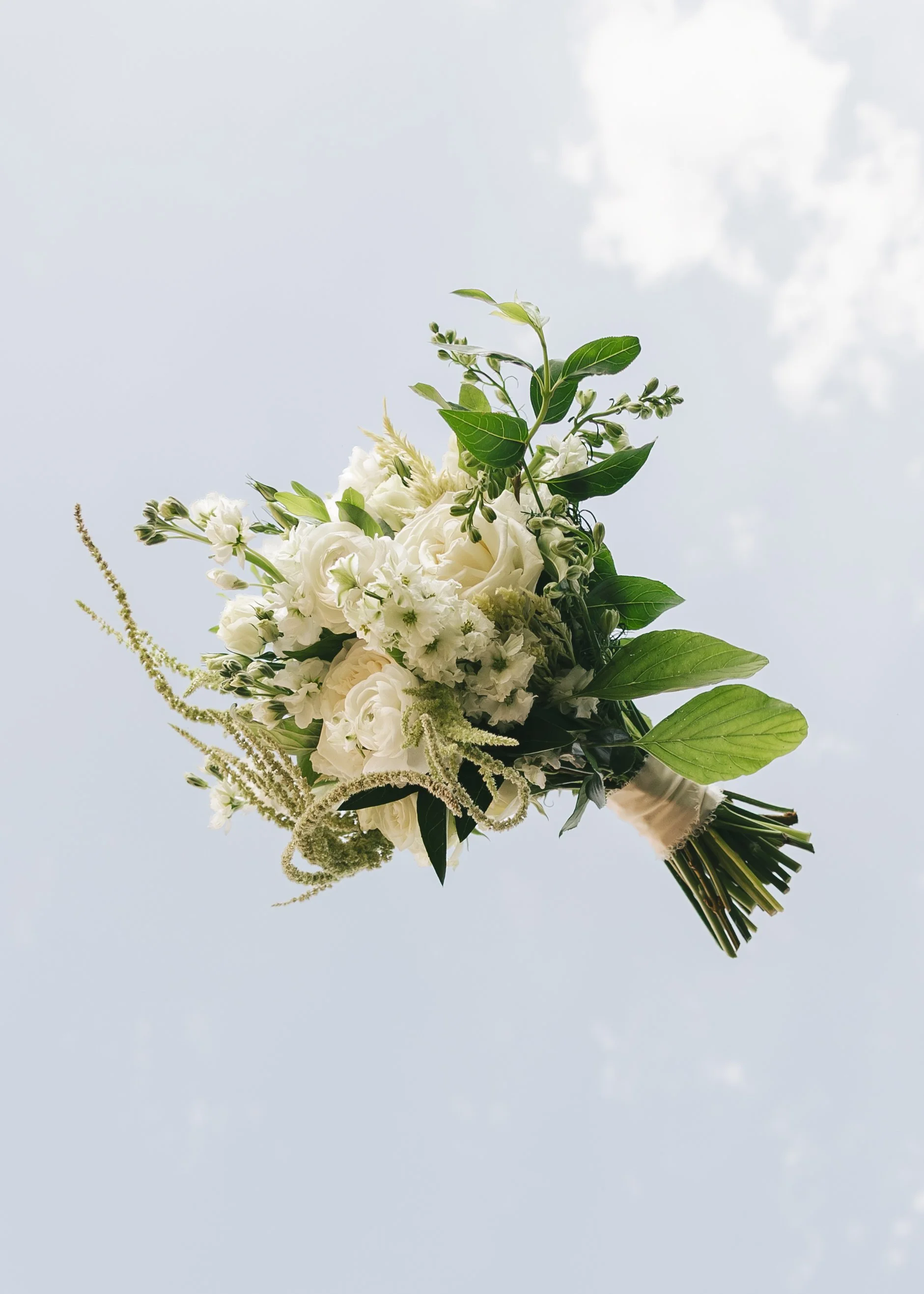 A bouquet of white flowers and green leaves, being tossed in the air for the new photo trend. 