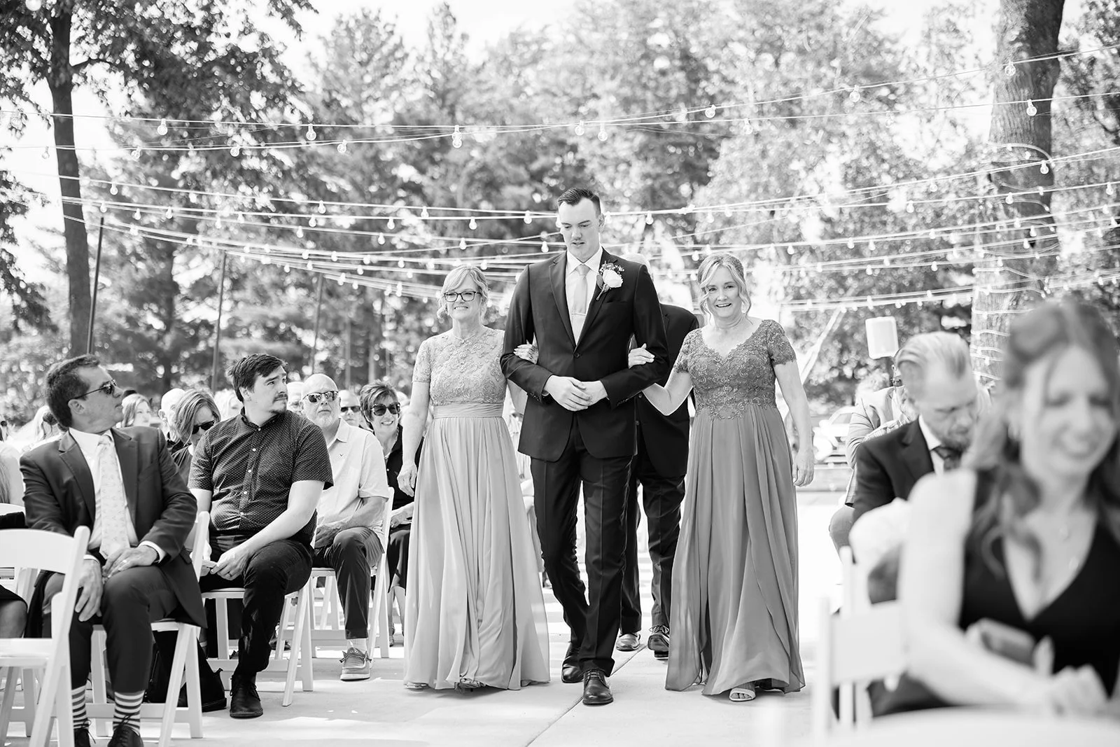 Groom walking down the aisle with two women during an outdoor wedding ceremony