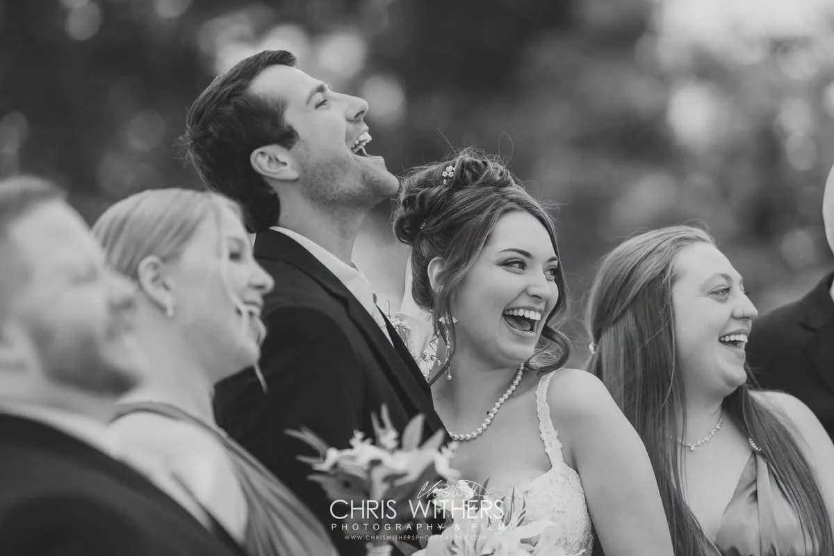 Group of people, including a newly married couple, smiling and laughing at a wedding celebration outdoors.