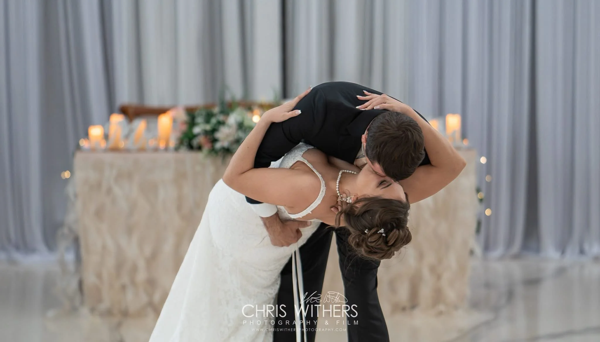 A bride and groom share a romantic dance at their wedding reception, with the groom dipping the bride and holding her close.