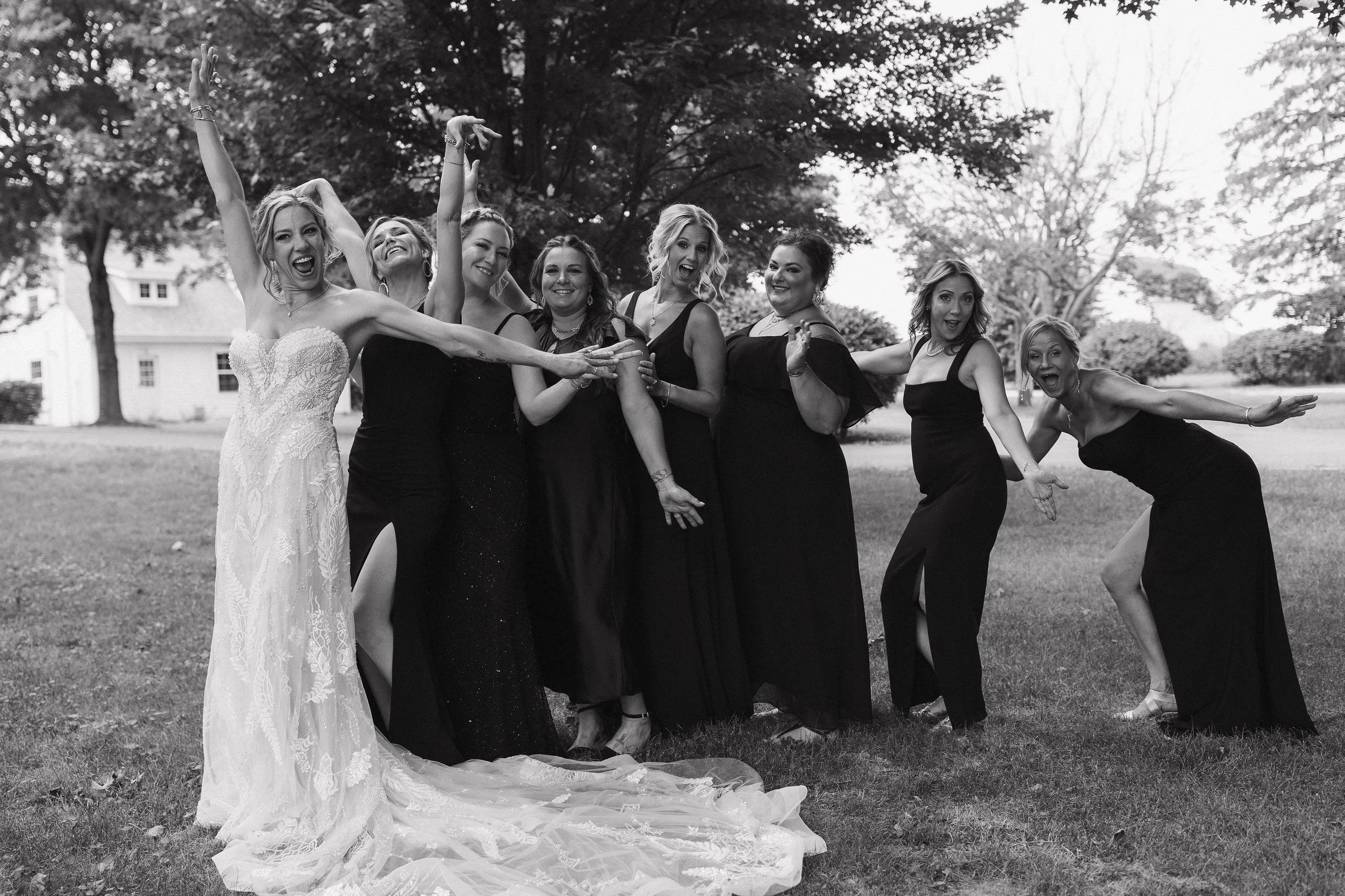 Group of women in formal dresses, celebrating outdoors on a grassy area with trees in the background.