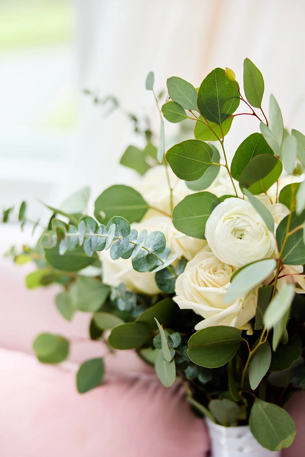 Bouquet of white roses and green eucalyptus leaves on a pink surface.
