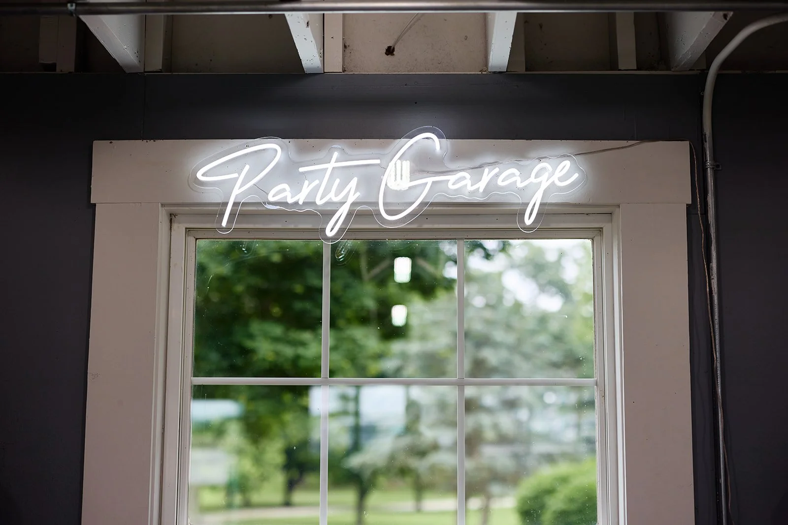 Neon sign reading 'Party Garage' above a window showing trees and greenery outside.