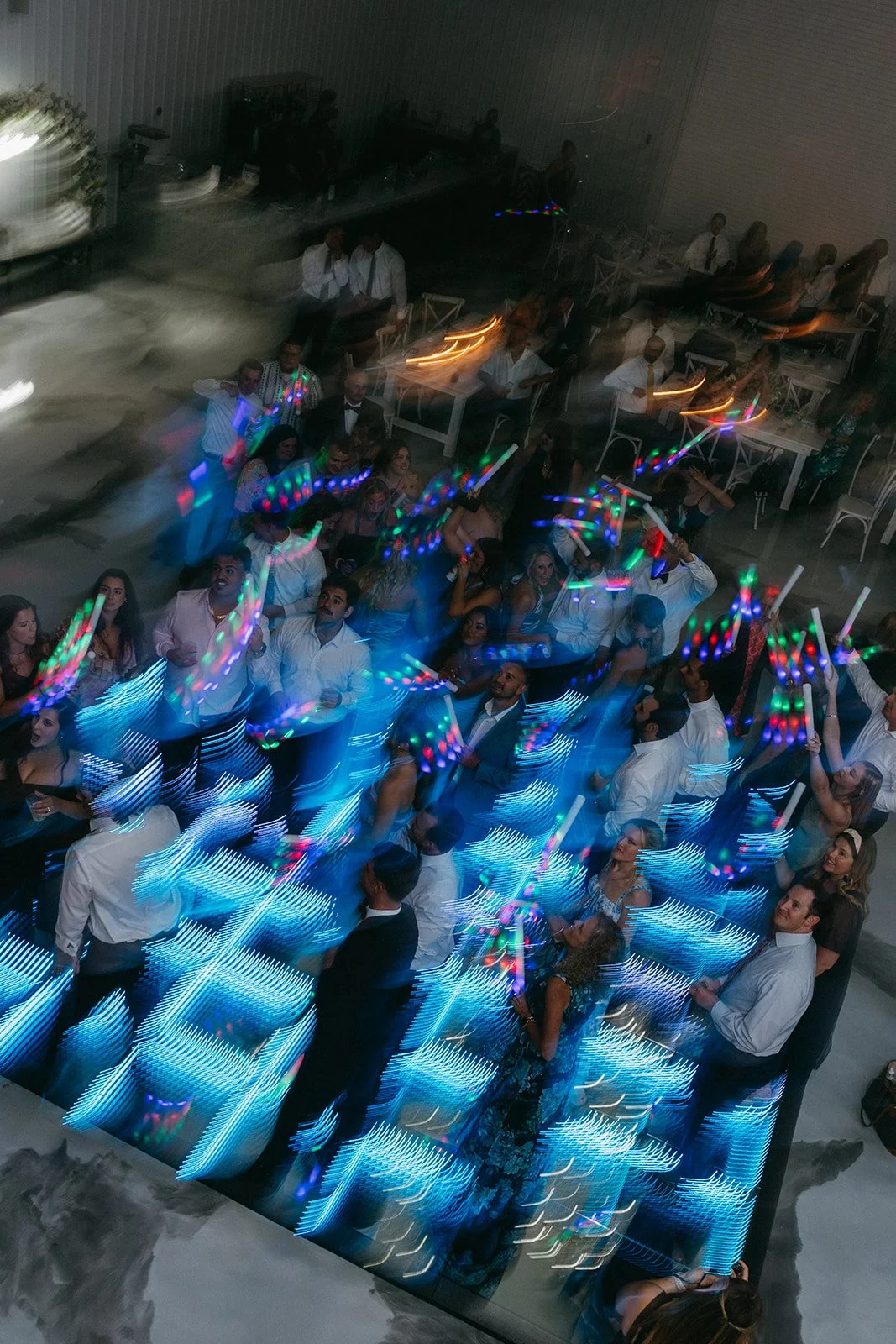 People dancing and celebrating at a party with colorful light streaks created by slow shutter photography, in an indoor event space.