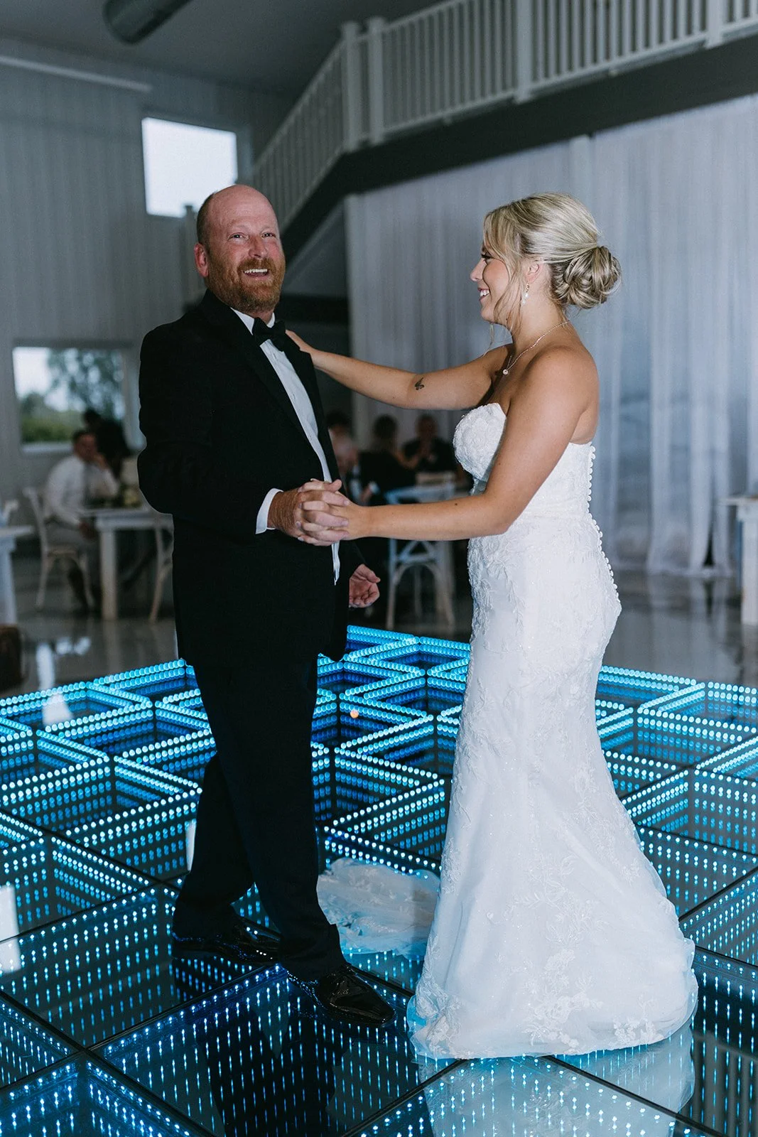 A bride and groom dancing on a light-up dance floor at their wedding reception, smiling and enjoying the moment.