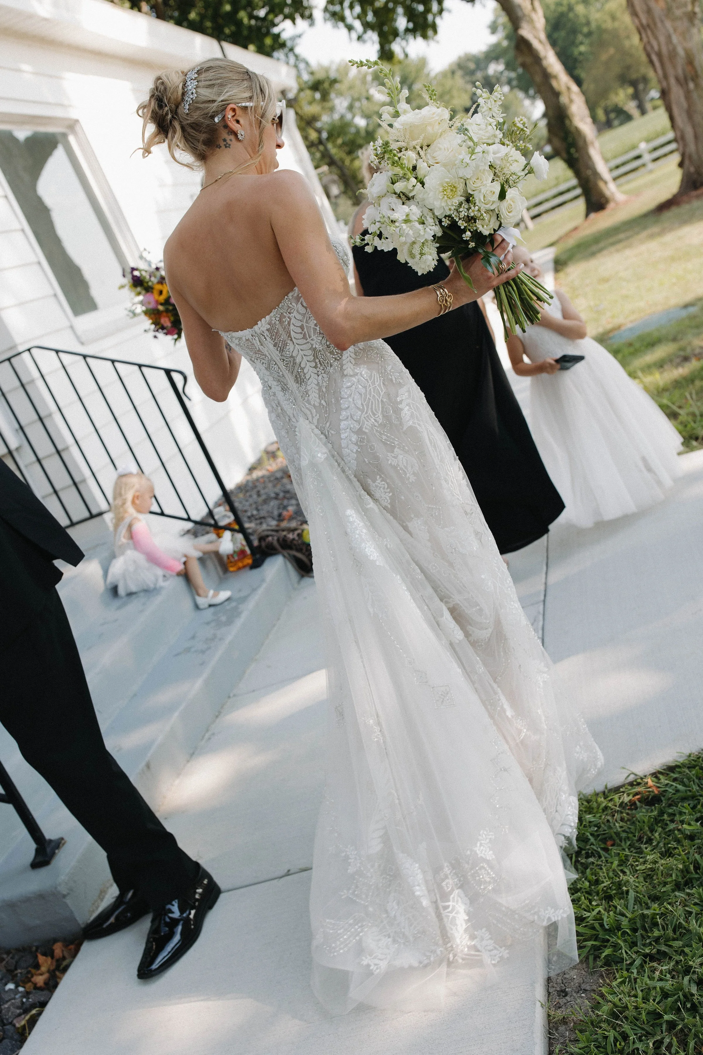 Bride in a white wedding gown holding a large bouquet of white flowers on her wedding day outdoors.