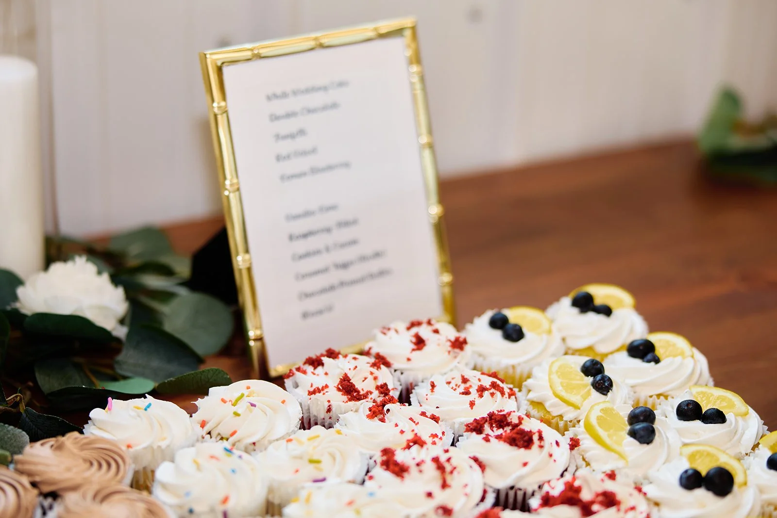Cupcakes with lemon slices and blueberries, decorated with whipped cream, on a wooden table with a blurred menu and greenery in the background.