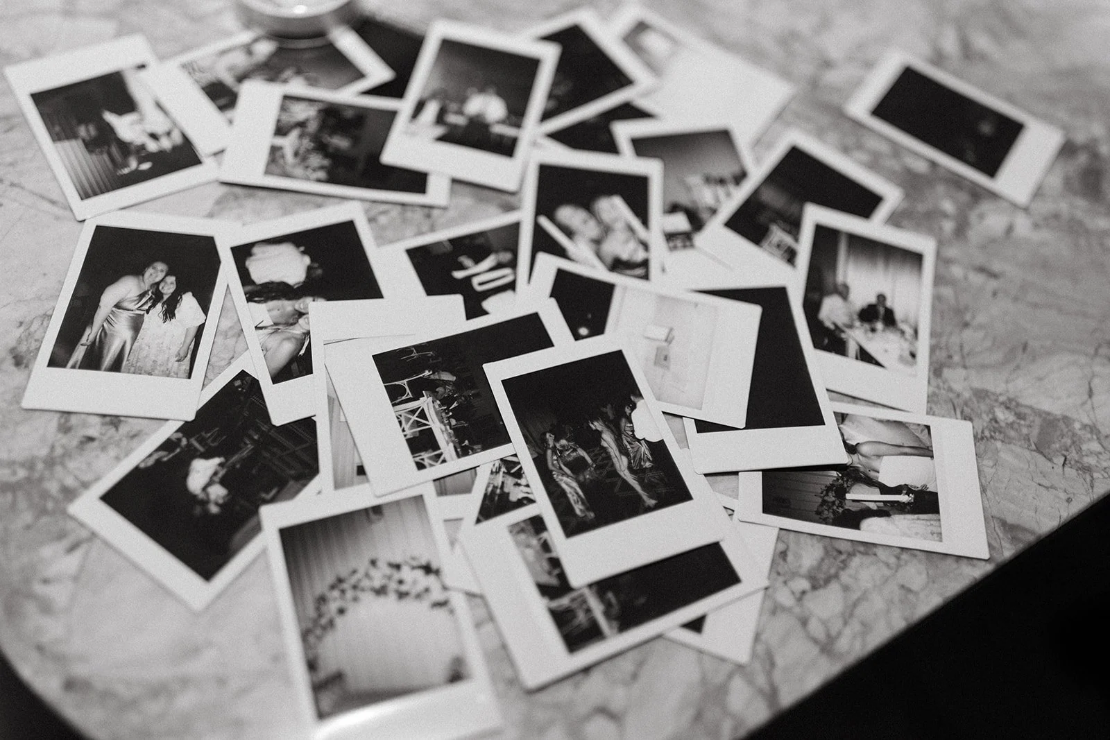 Scattered black-and-white instant photos of a wedding celebration on a marble surface.