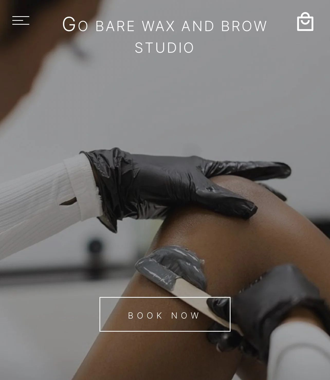 A person getting a waxing treatment on their leg in a studio, with a gloved hand applying wax.