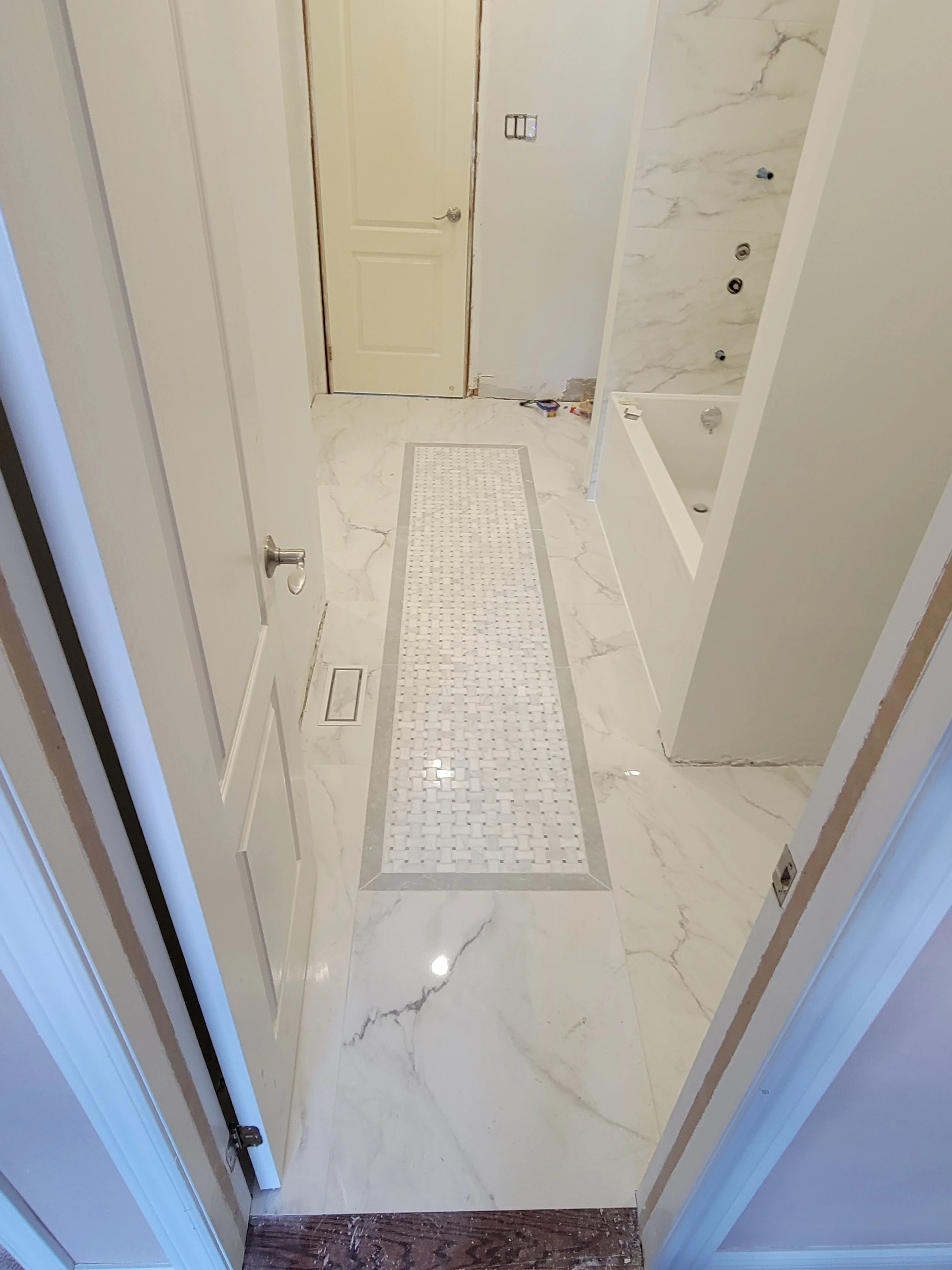 Newly renovated bathroom with marble floor tiles, a white paneled door, and a bathtub with a marble surround.
