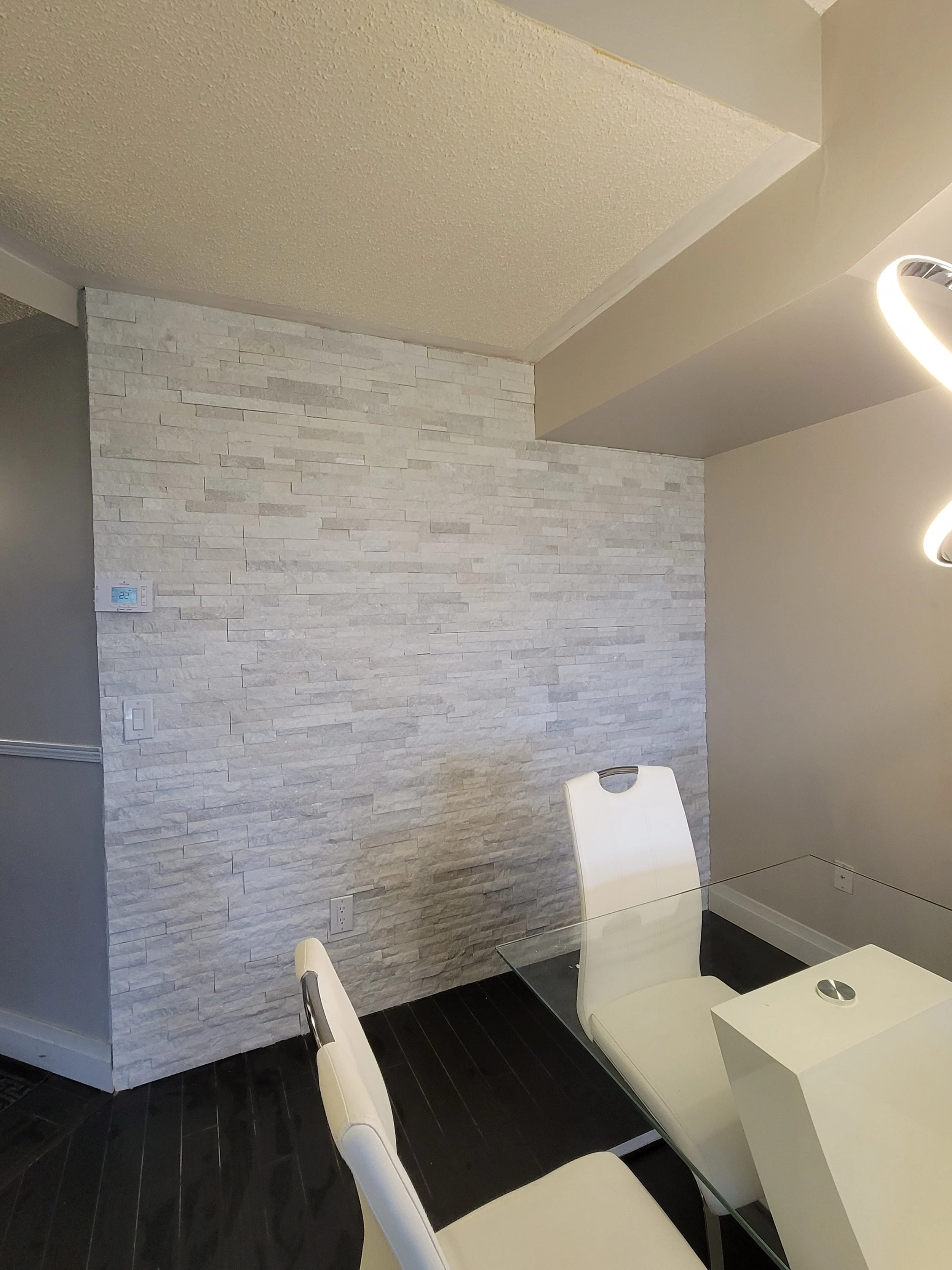 Modern dining room with textured stone accent wall, glass table, and white chairs.