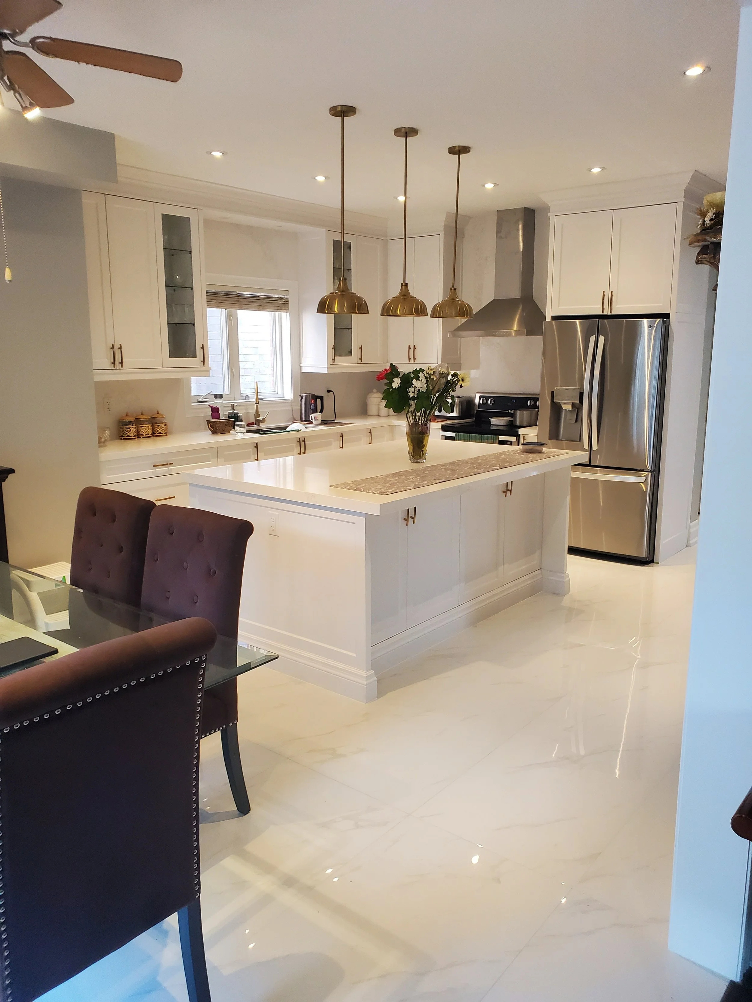 Modern kitchen with white cabinetry, island, stainless steel appliances, gold pendant lights, and a vase of flowers on the counter.