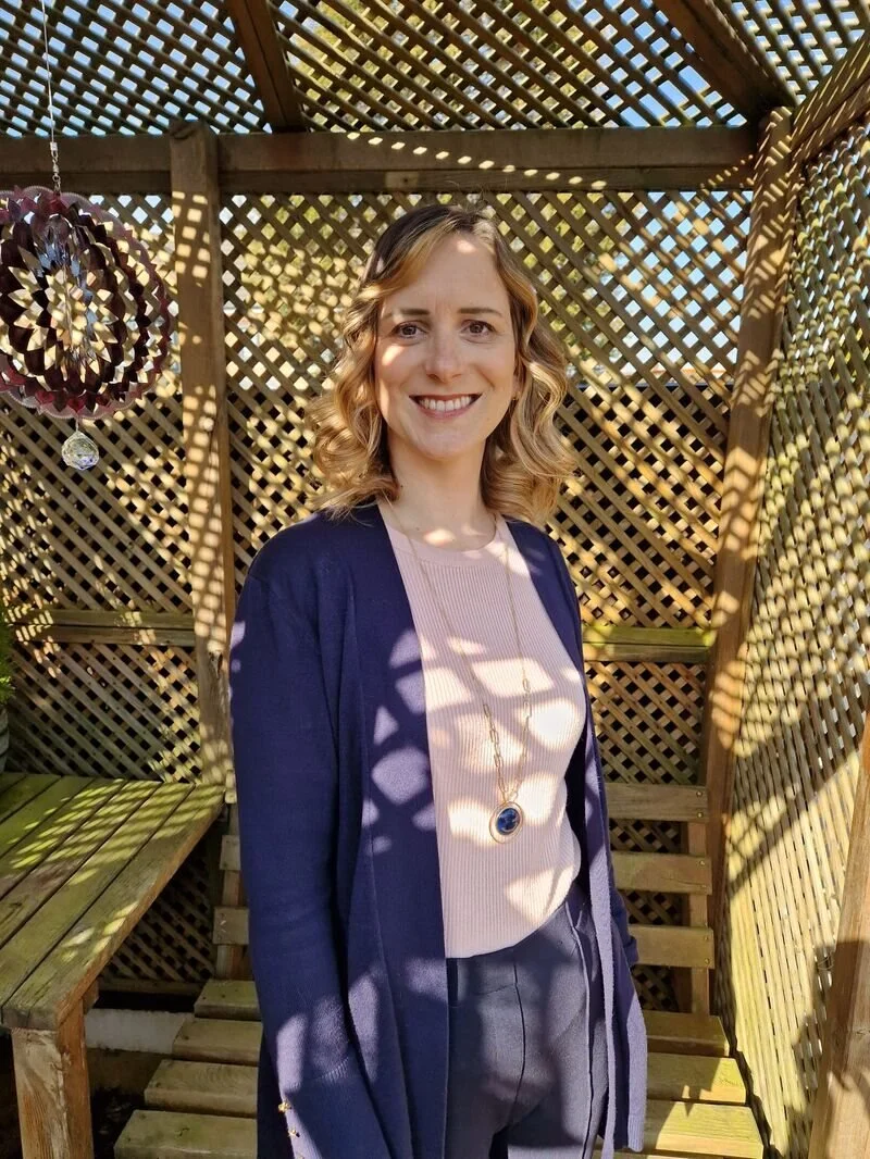 Kelly standing outside under a garden shelter smiling at the camera