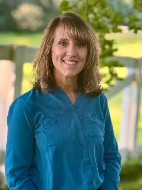 Heidi Simon wearing a blue shirt with green trees and field in background.