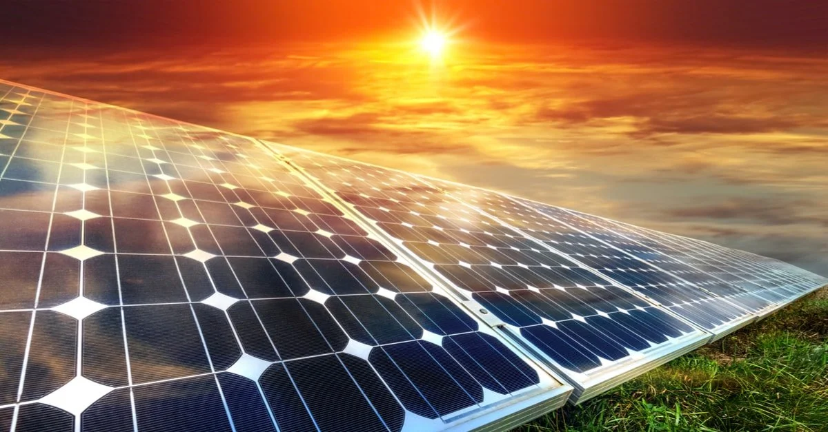 Solar panels in a grassy field with a bright orange sunset.