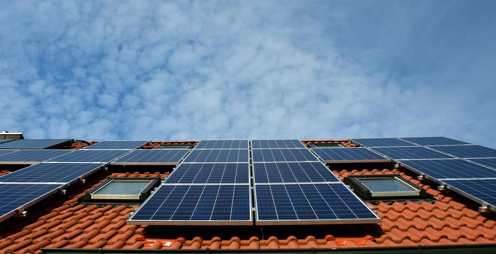 Solar panels on a red-tiled roof under a partly cloudy sky.
